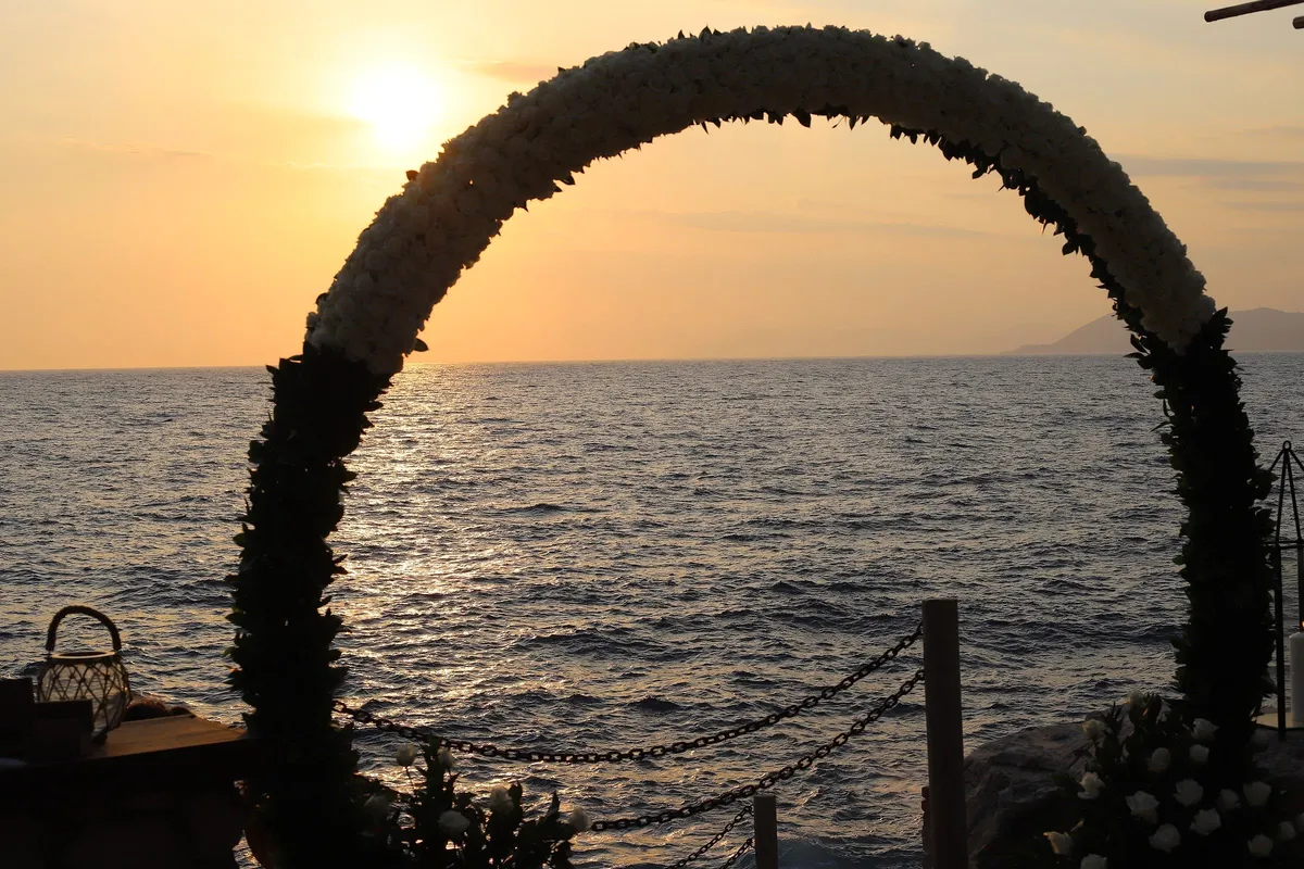 A floral arch at the end of the pier, framing the sun as it lowers over the sea.